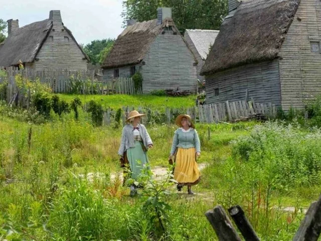 Two women in historical dress walking through a village.