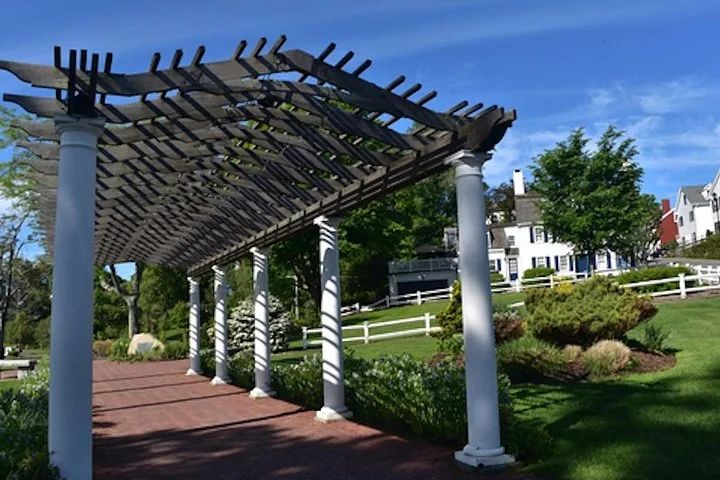 A wooden pergola over a brick path in a park.